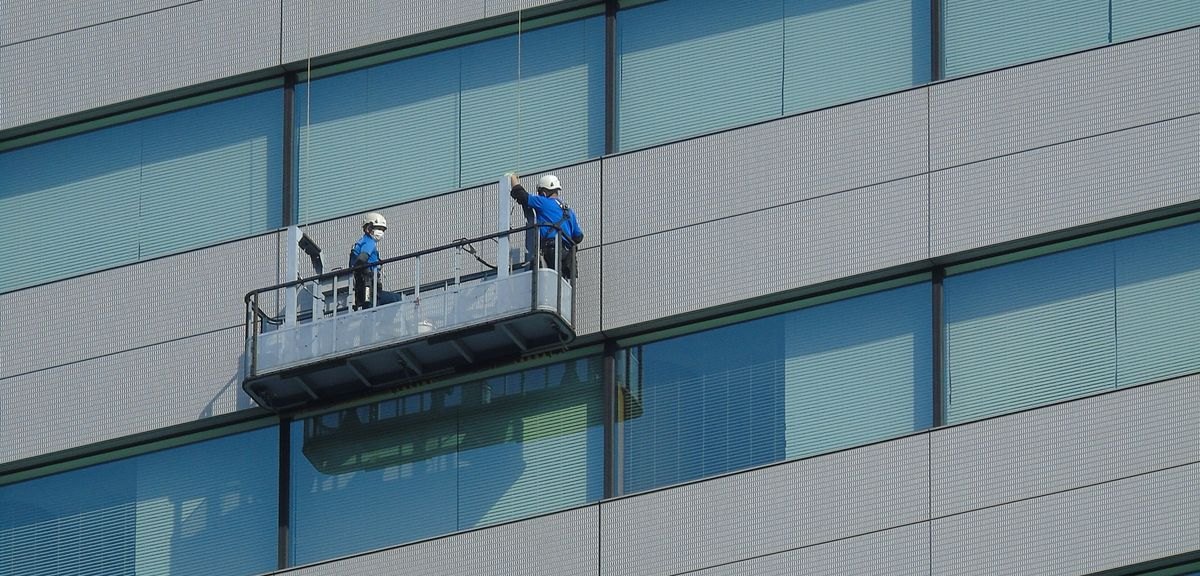 Glazenwassers reinigen vanaf een hangbrug de ramen van een kantoorpand